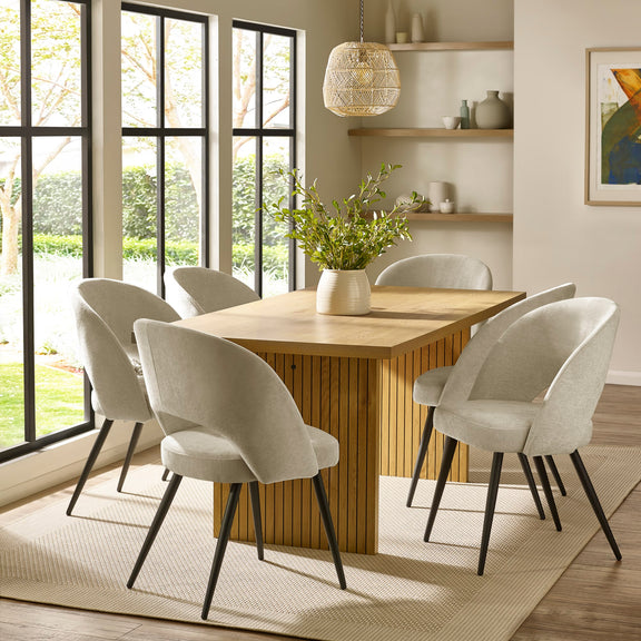 Dining room with wooden table and white chairs near large windows.