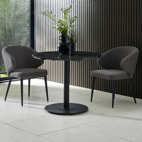 Two gray chairs around a black round table with a vase of plants on a tiled floor.