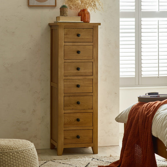 Wooden tall dresser with multiple drawers in a bedroom setting.