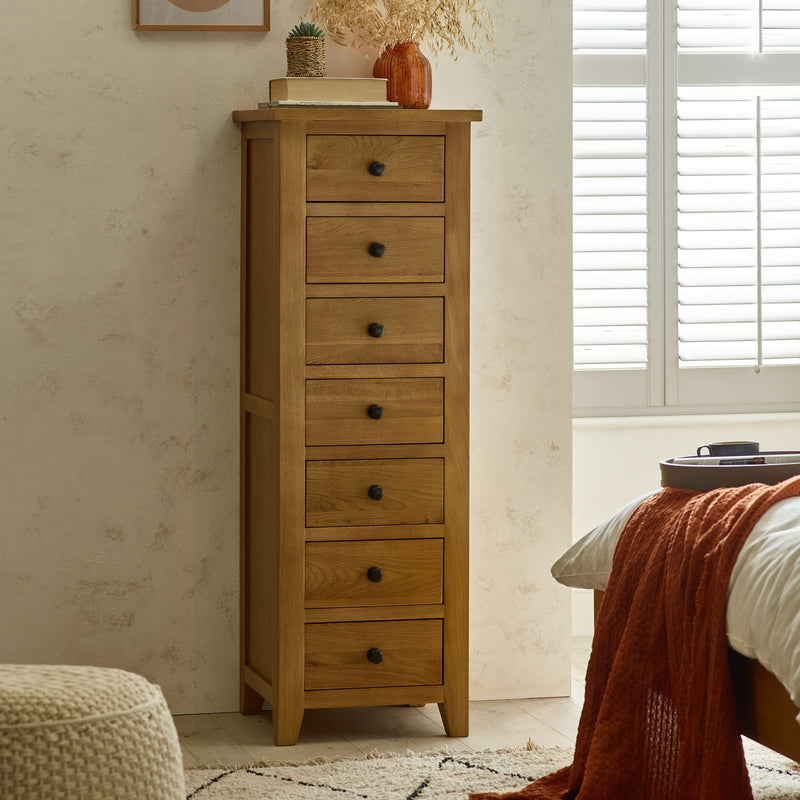 Wooden tall dresser with multiple drawers in a bedroom setting.