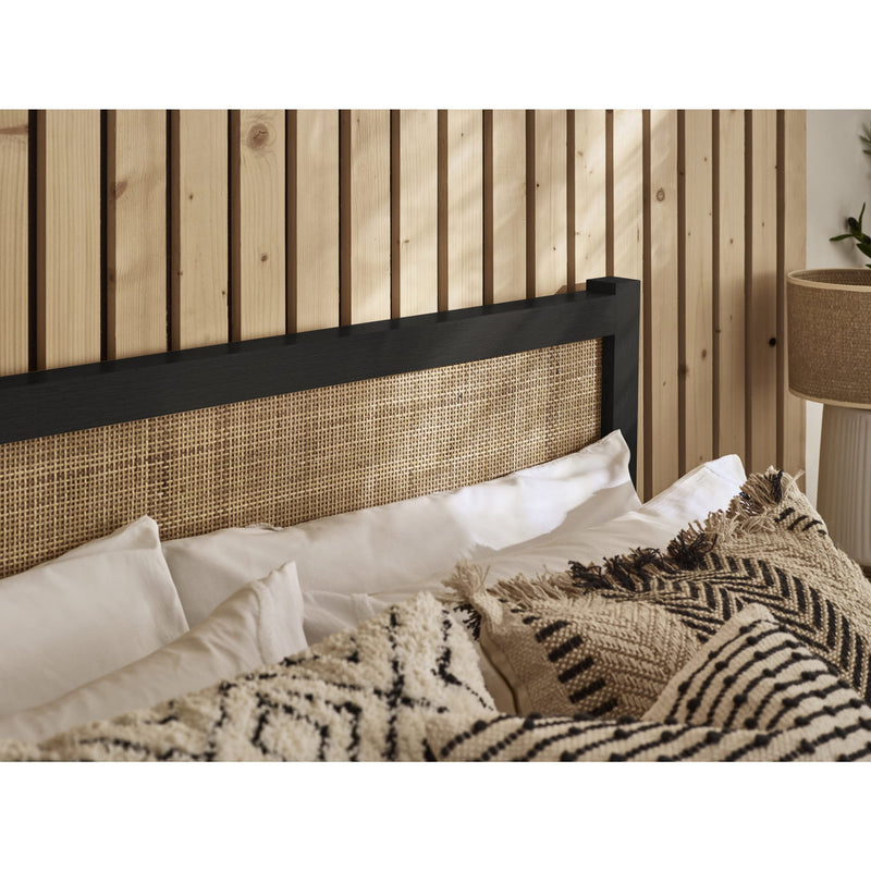 Bed with wicker headboard and textured bedding against a wooden paneled wall.