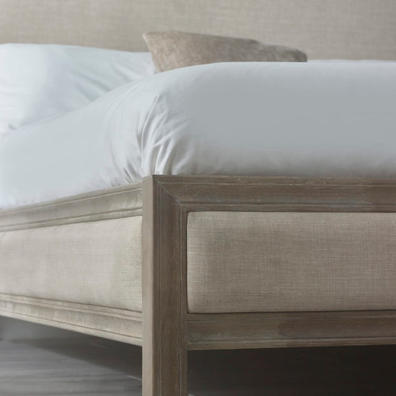 Beige upholstered bed with white bedding in a neutral room setting