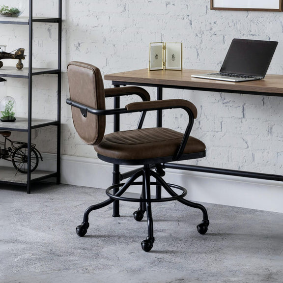 Brown office chair in front of a wooden desk with a laptop, against a white brick wall.