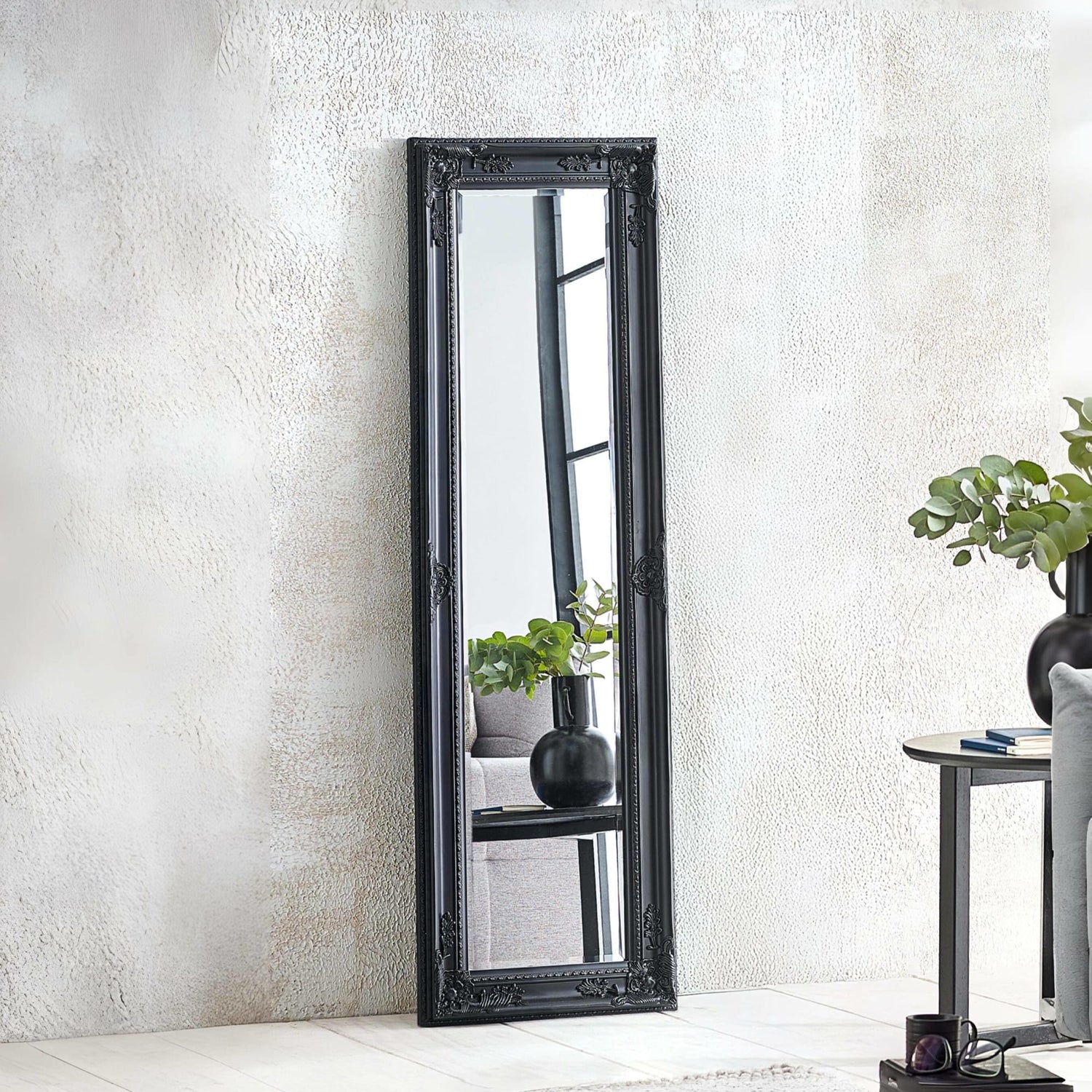 Black framed mirror leaning against a white wall with decorative elements.