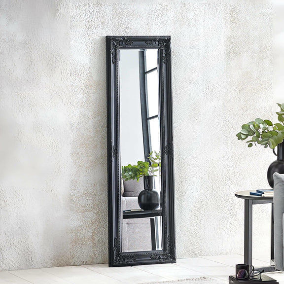Black framed mirror leaning against a white wall with decorative elements.