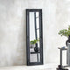 Black framed mirror leaning against a white wall with decorative elements.