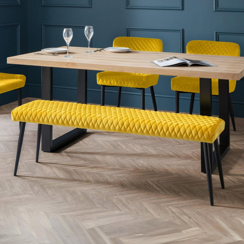 Dining area with a wooden table, yellow chairs, and bench against a blue wall.