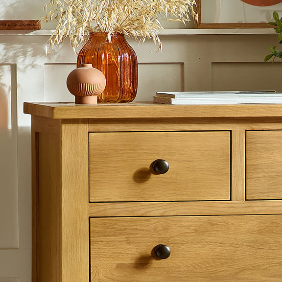 Wooden dresser with two drawers, an orange vase, and a small pink ceramic item on top.