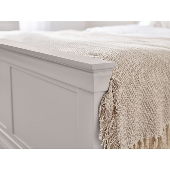 Beige woven blanket with fringes draped over a white bed frame.