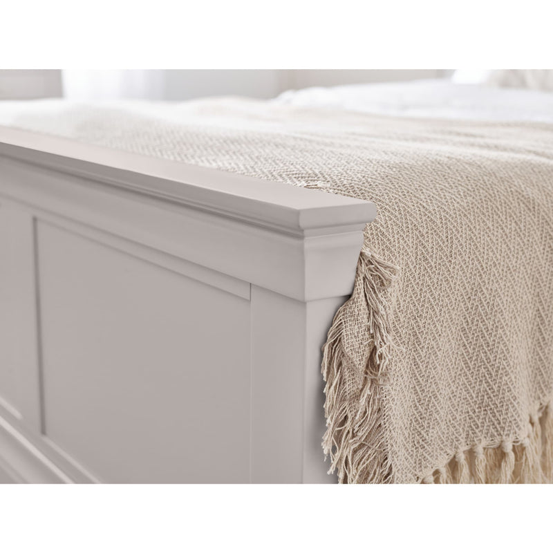 Beige woven blanket with fringes draped over a white bed frame.