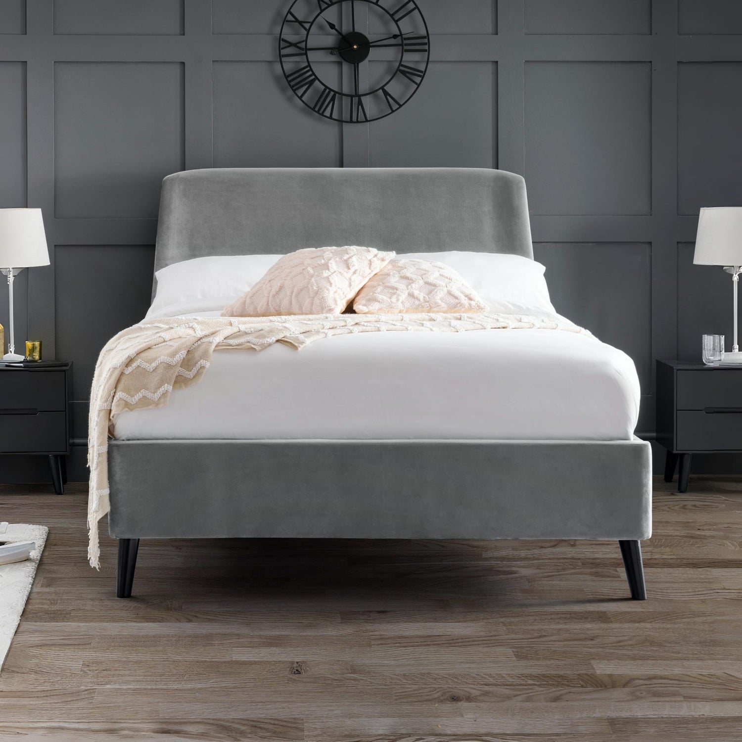 Gray upholstered bed with white bedding in a room with dark gray walls and wooden flooring.