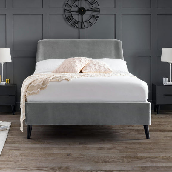 Gray upholstered bed with white bedding in a room with dark gray walls and wooden flooring.