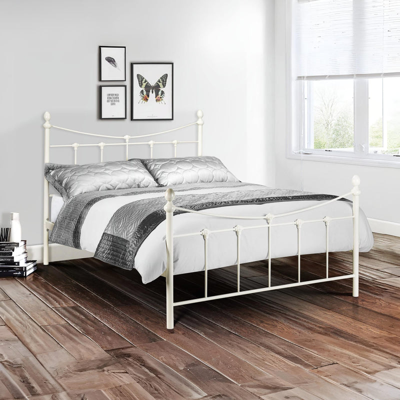 White metal bed with gray bedding in a room with wooden flooring and framed pictures on the wall.