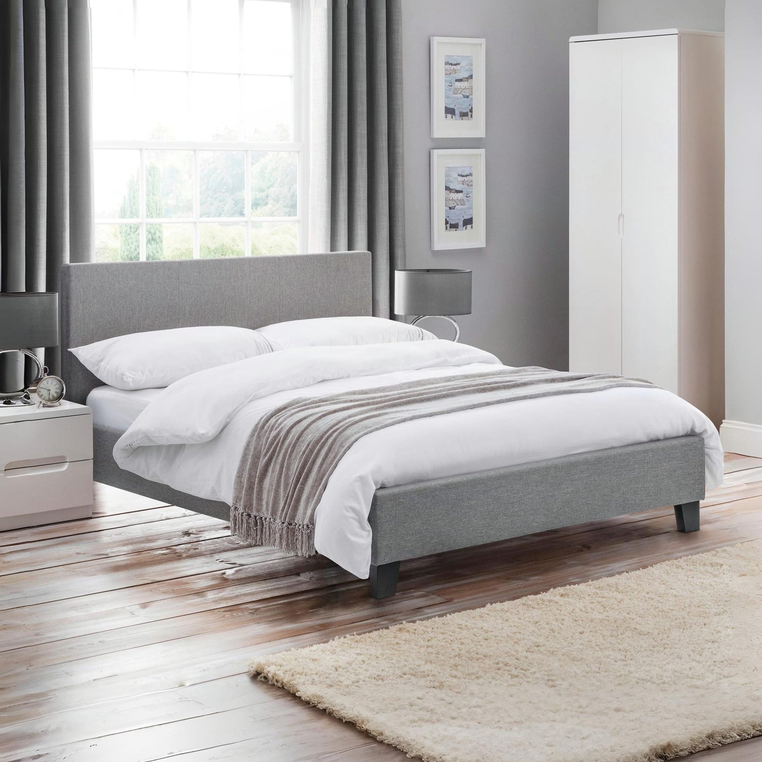 Modern bedroom with gray upholstered bed, white bedding, and wooden flooring.
