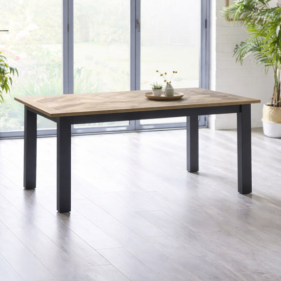 Wooden dining table with black legs in a bright room with large windows.