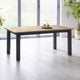 Wooden dining table with black legs in a bright room with large windows.