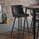 Gray quilted bar stools in front of a wooden table against a brick wall.