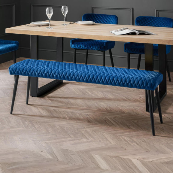Dining room setup with a wooden table, blue upholstered chairs, and bench on a herringbone wood floor.