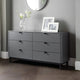 Gray dresser with black handles in a room with a mirror and framed pictures.