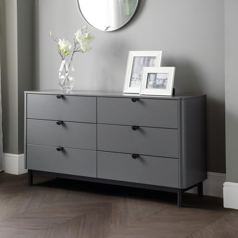 Gray dresser with black handles in a room with a mirror and framed pictures.