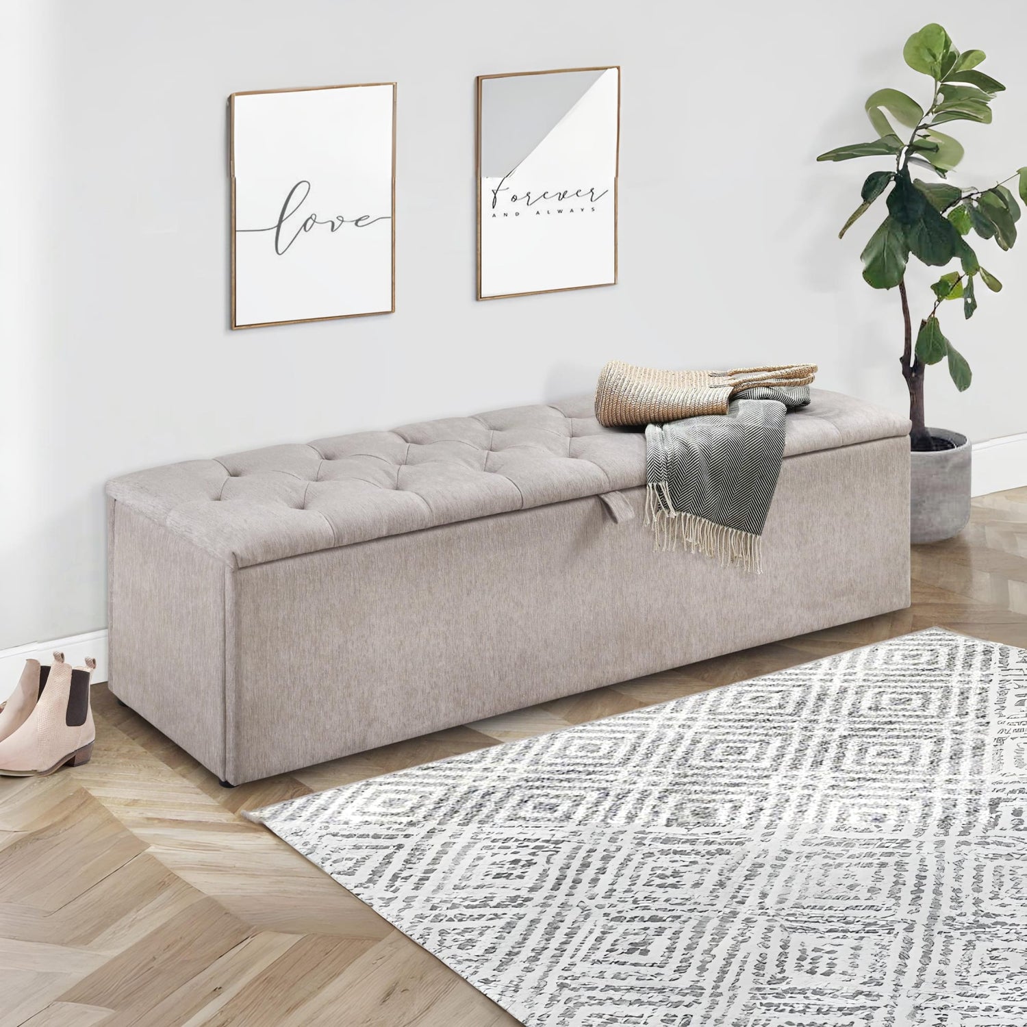 Gray upholstered storage bench in a room with a plant, rug, and wall art.