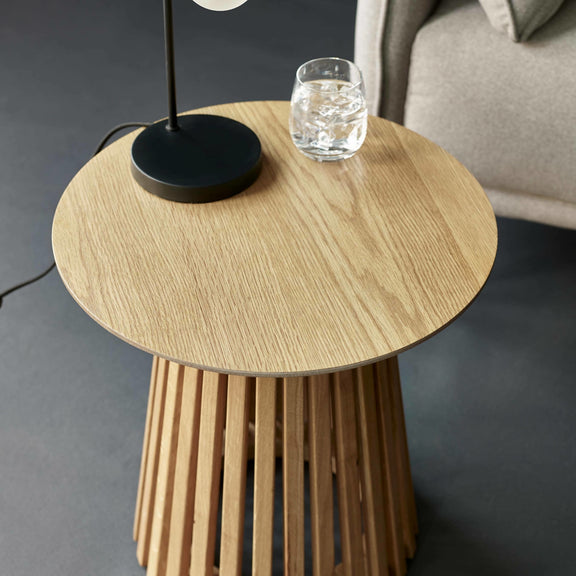 Wooden side table with a black lamp and glass of water on a dark gray background