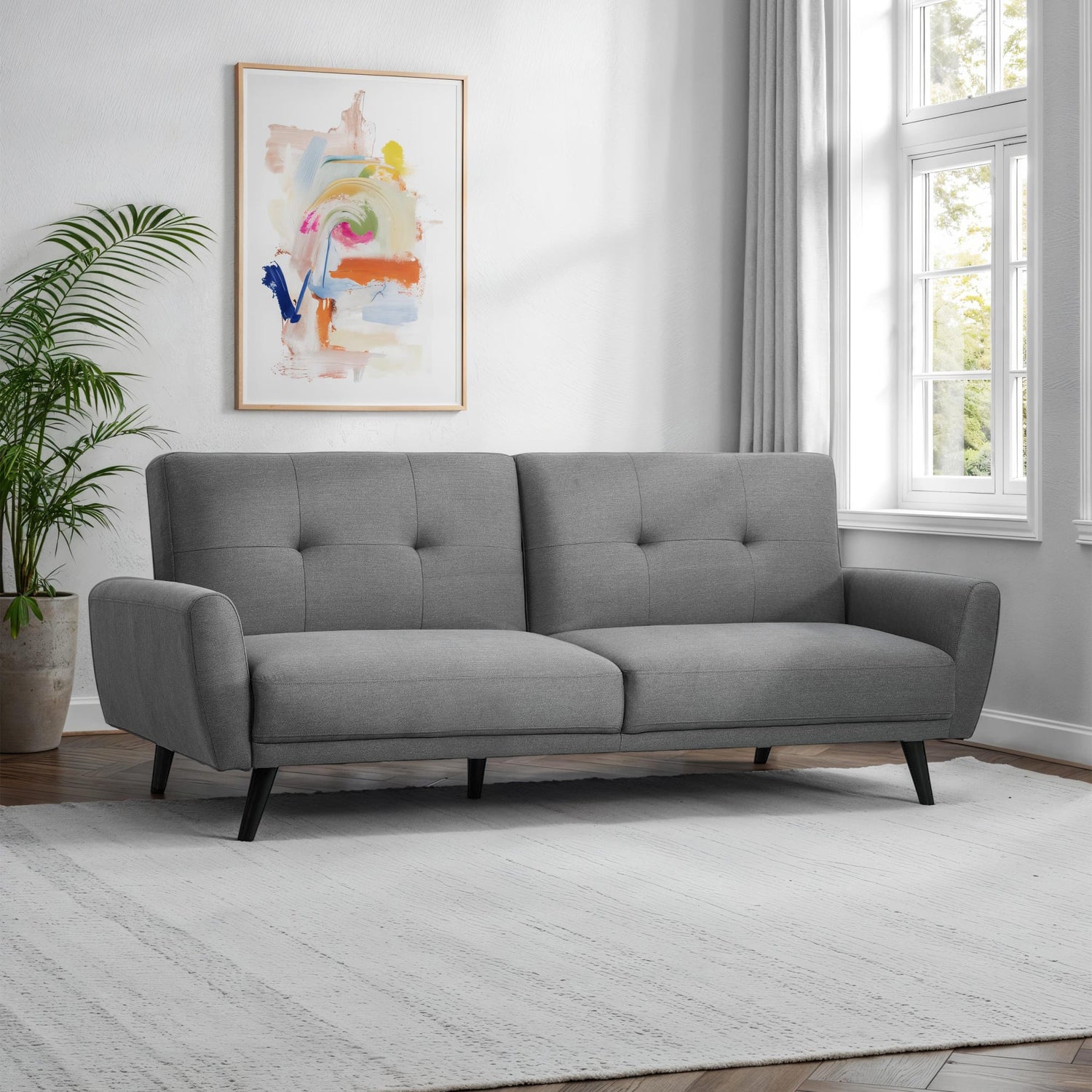 Gray sofa in a room with a colorful abstract painting on the wall and a plant.