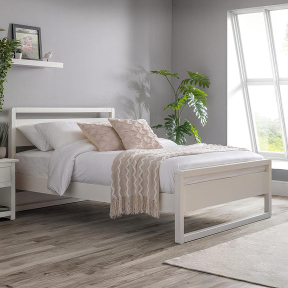 White bed frame with bedding in a bedroom setting with plants and a window.