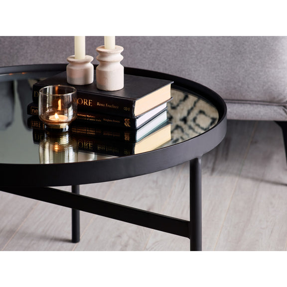 Round glass coffee table with books and candles in a living room setting