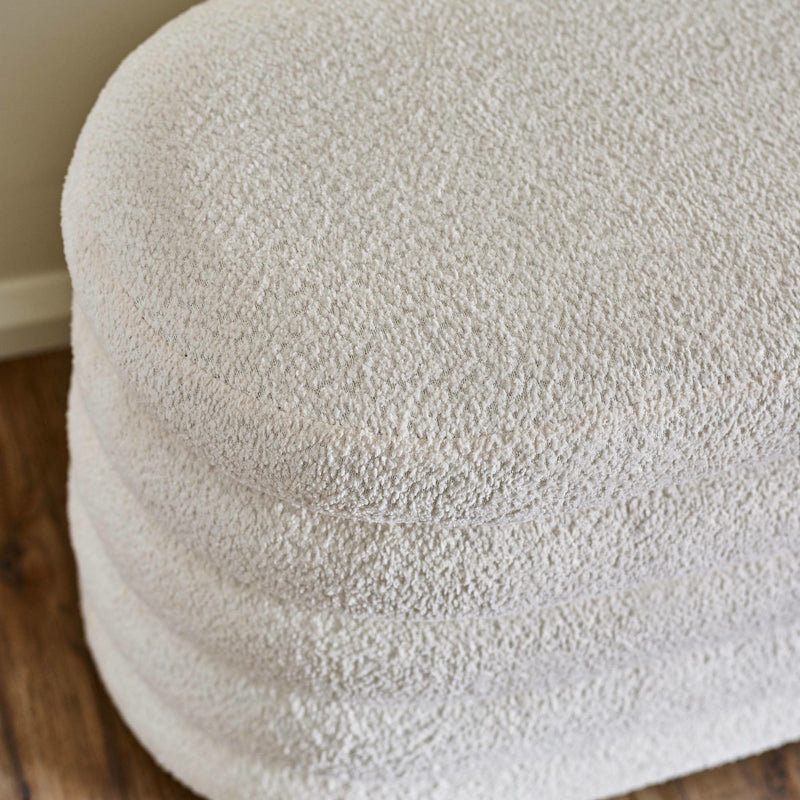 Close-up of a textured beige ottoman on a wooden floor.