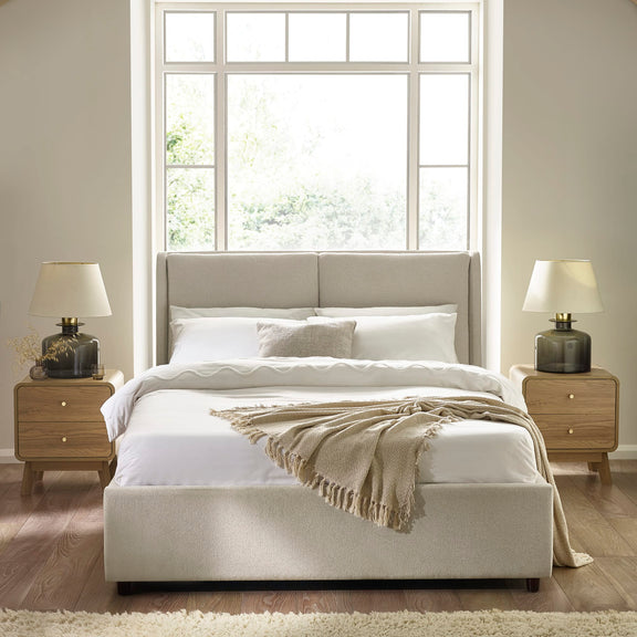 Neatly made bed with beige headboard and bedding in a bright bedroom.