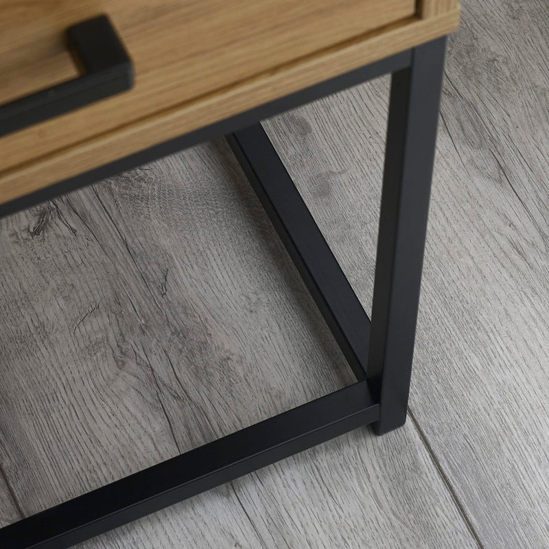 Close-up of a wooden table with a black metal leg on a gray wooden floor.