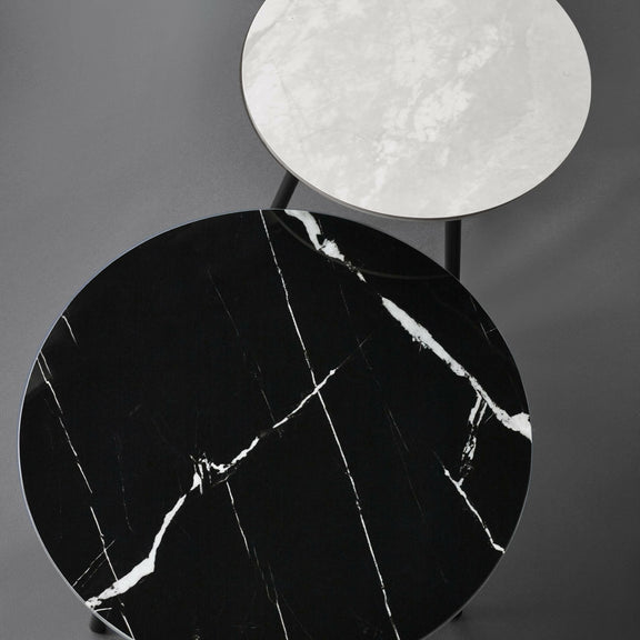 Two round marble surfaces, one black with white veins and one white, on a gray background.