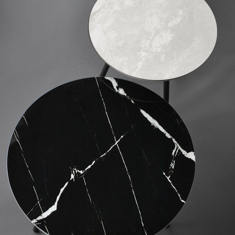 Two round marble surfaces, one black with white veins and one white, on a gray background.