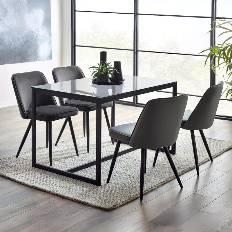 Dining table set with four chairs in a modern room with large windows.