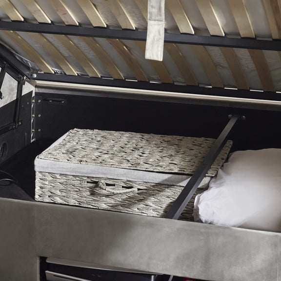 Storage compartment with a woven box and white blanket inside a vehicle with an open roof.