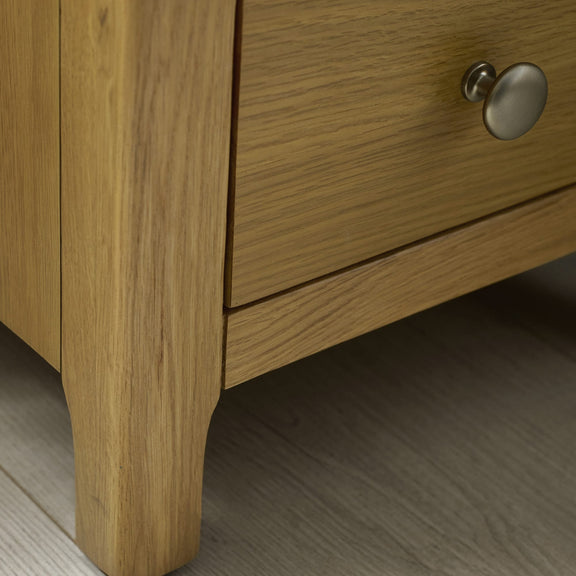 Close-up of a wooden drawer with a metal handle on a light wood floor.