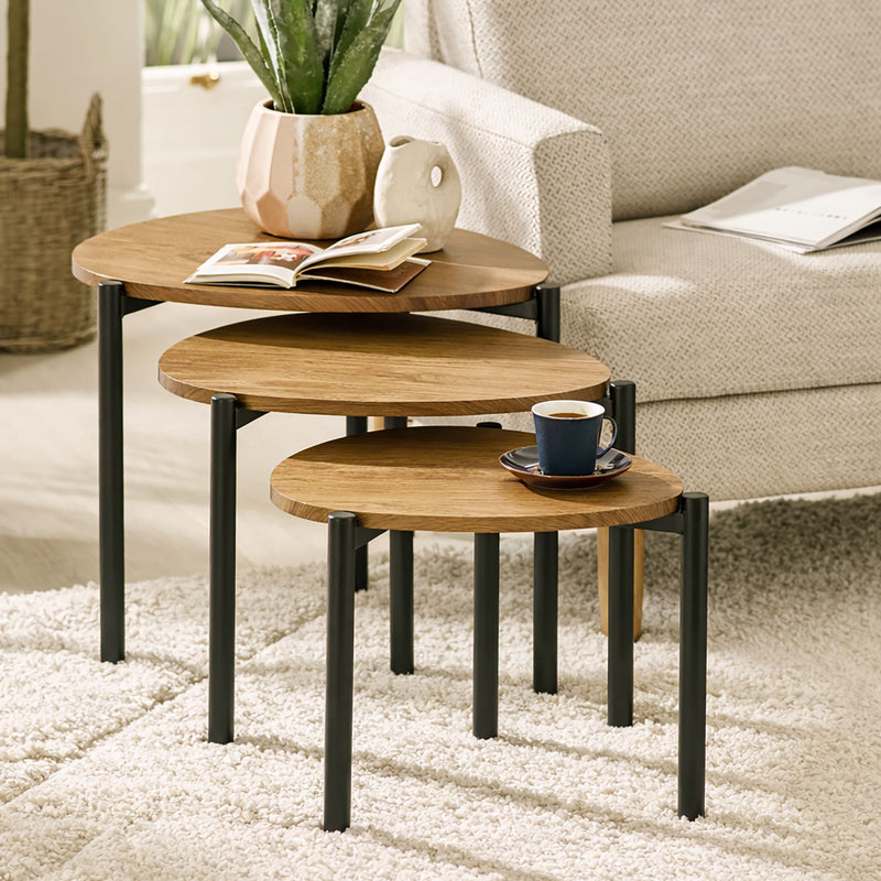 Set of three wooden nesting tables with black legs in a living room setting.