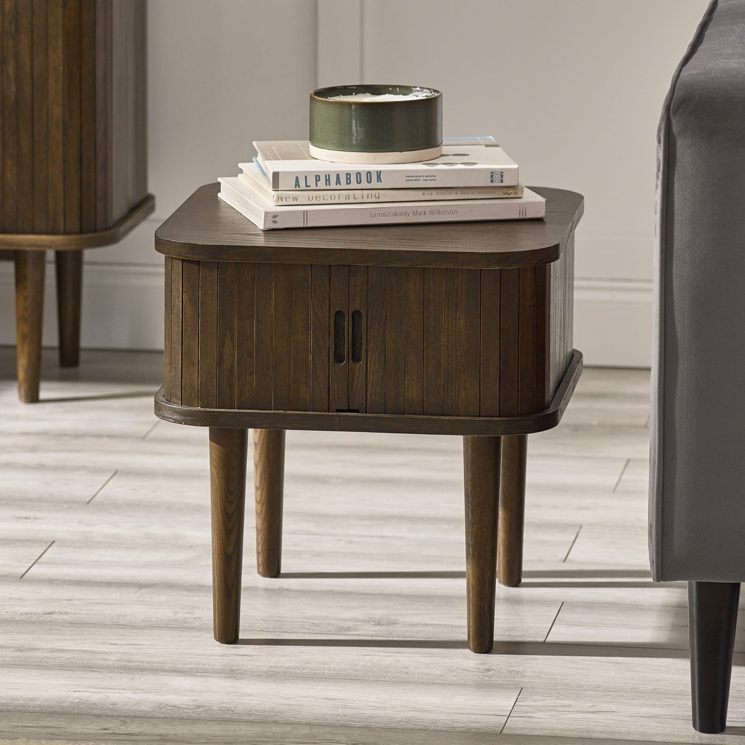 Wooden side table with books and a plant on a wooden floor.