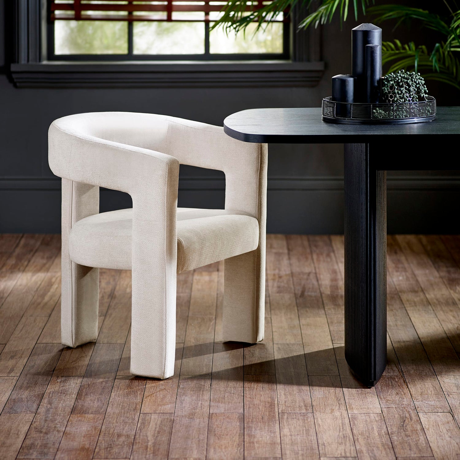 Beige chair next to a black dining table with decorative items on a wooden floor.