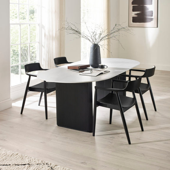 Modern dining room with a white oval table and black chairs.