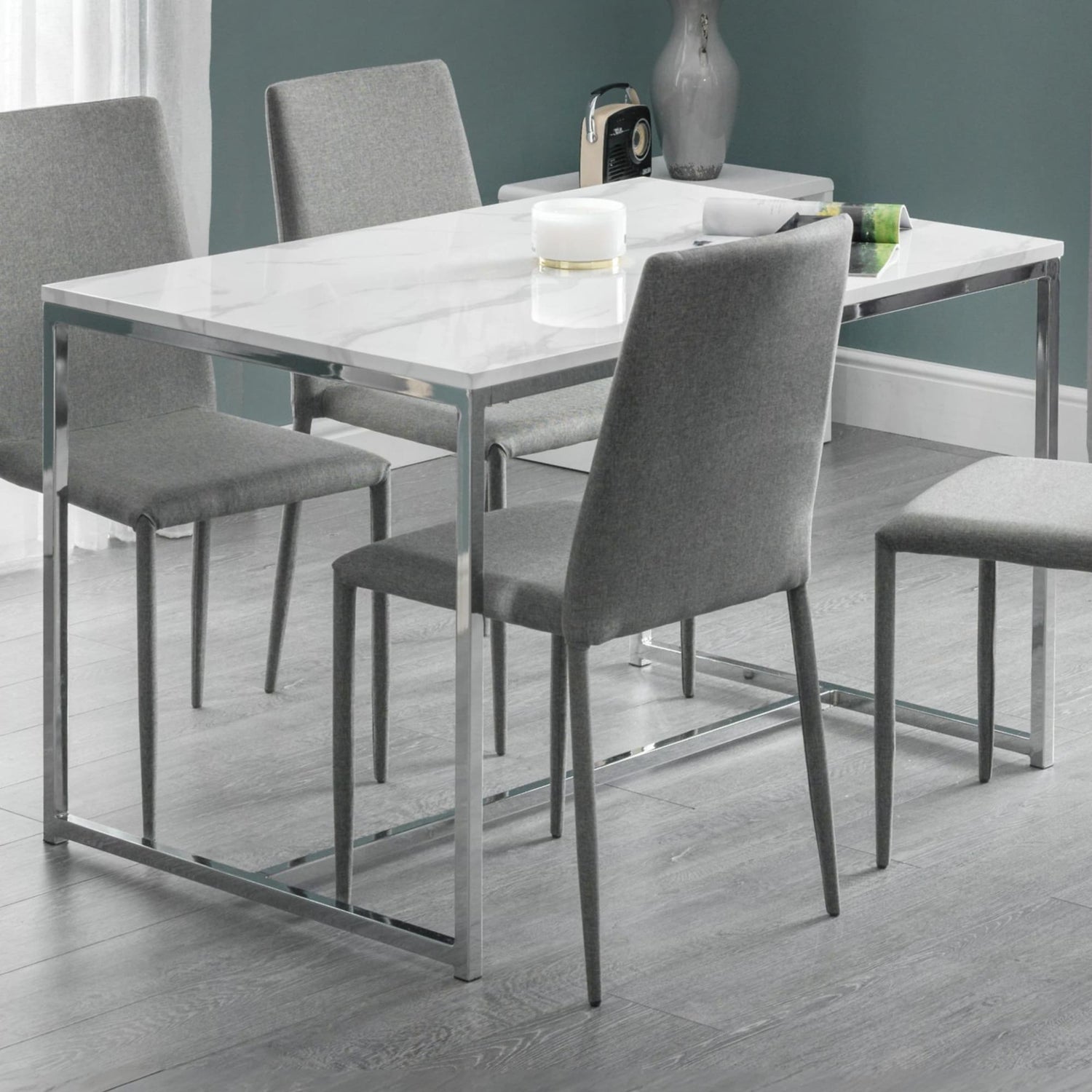 Dining table with four gray chairs in a room with a teal wall.