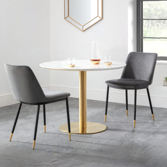 Round dining table with gold base and two gray chairs in a modern room.