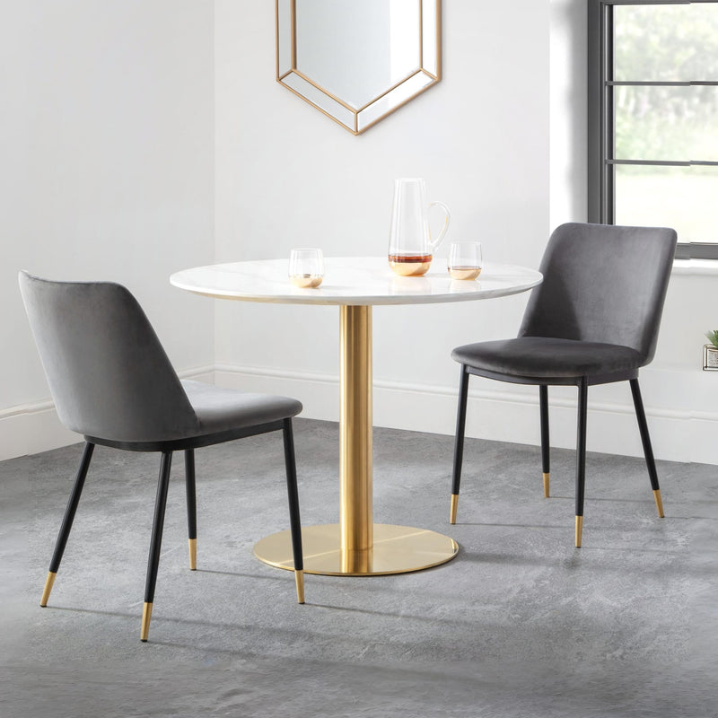 Round dining table with gold base and two gray chairs in a modern room.