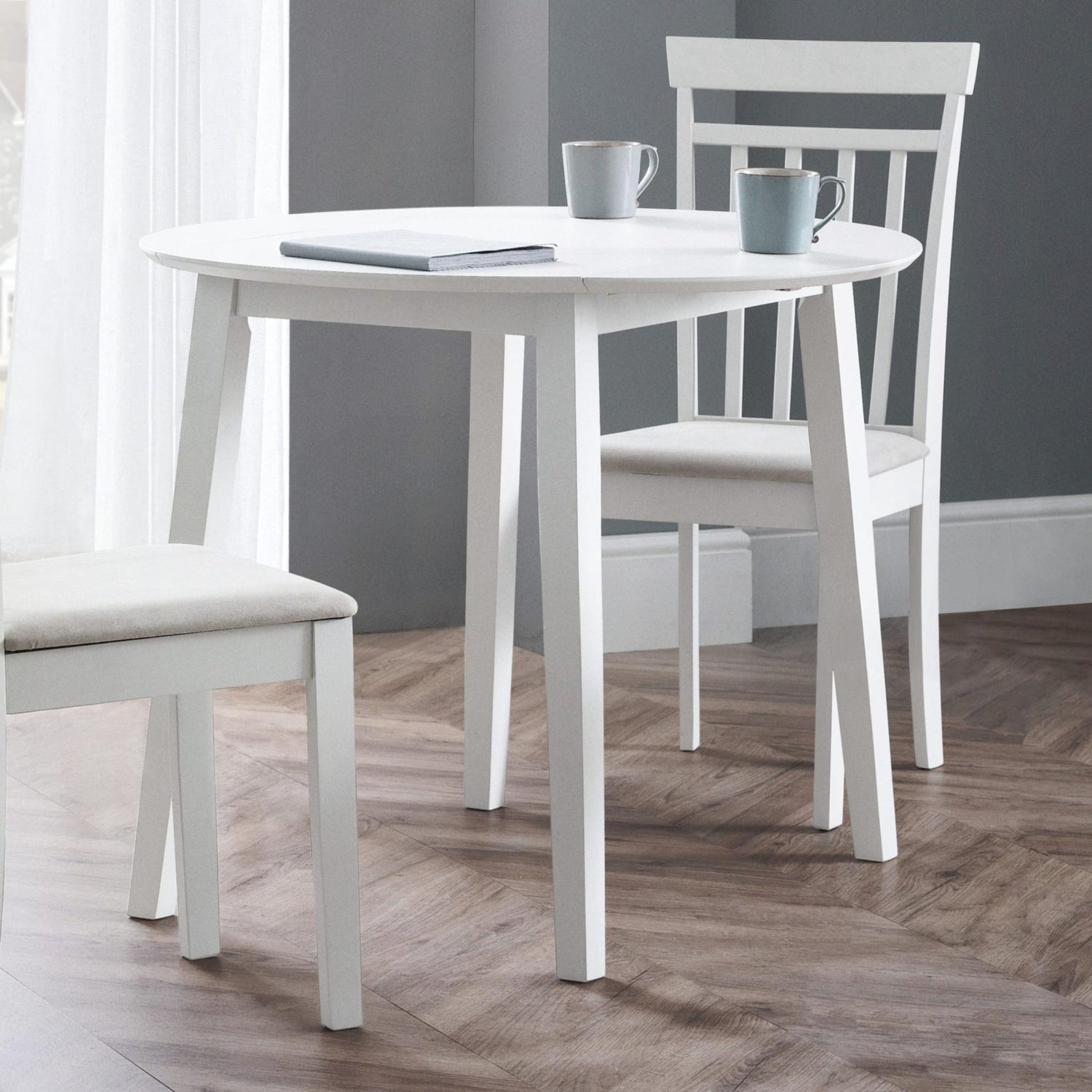 White dining table with two chairs in a room with gray walls and wooden flooring.