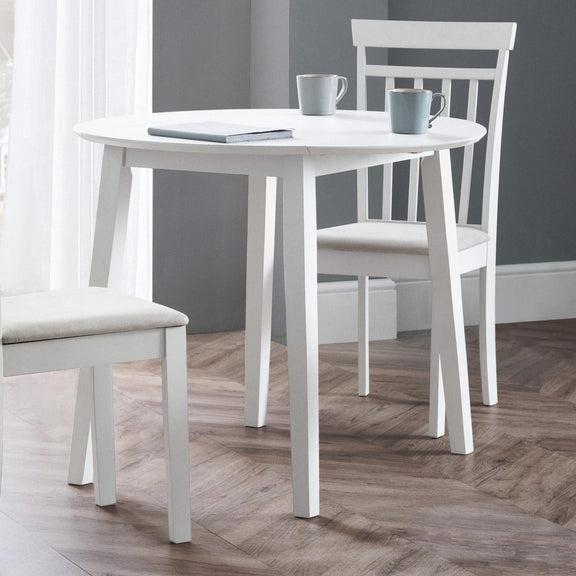 White dining table with two chairs in a room with gray walls and wooden flooring.