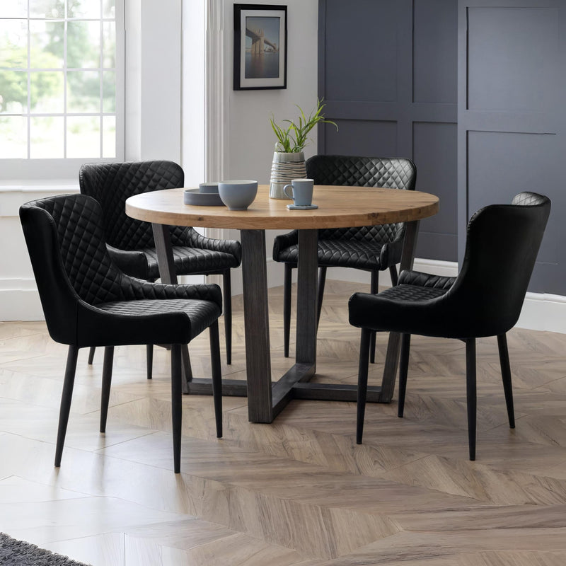 Dining room with a round wooden table and black chairs on a wooden floor.