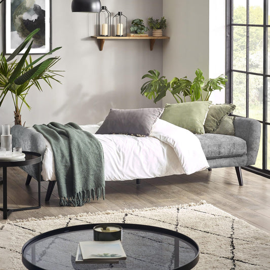 Modern living room with a gray sofa, white bedding, and decorative plants.