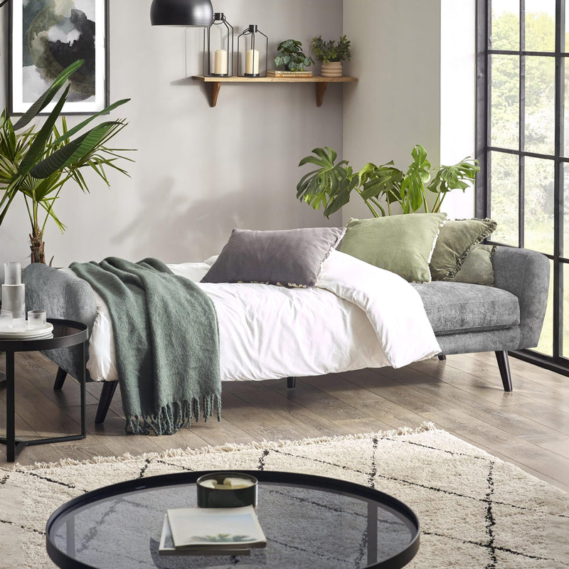 Modern living room with a gray sofa, white bedding, and decorative plants.
