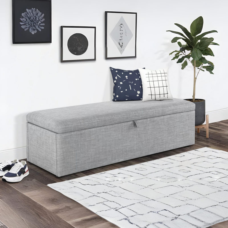 Gray storage bench with cushions in a room with a plant and framed art on the wall.